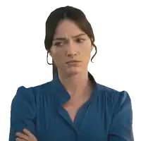 a woman in a blue shirt has her arms crossed and a serious look on her face