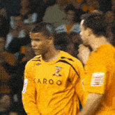 a man wearing a yellow karoo shirt stands in front of a crowd