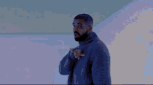 a man with a beard is wearing a gray sweater and pointing at something .