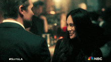 a man and a woman are looking at each other with the nbc logo in the background