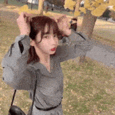 a woman is standing in front of a tree in a park and adjusting her hair .
