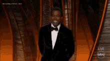 a man in a tuxedo stands on a stage in front of a live abc logo