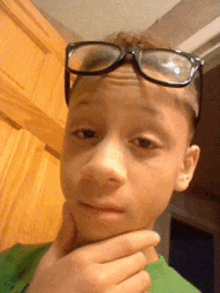 a young boy wearing glasses and a green shirt looks at the camera