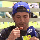 a man wearing a fox sports hat is eating a sausage