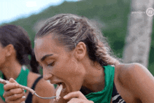 a woman is eating something with a fork while wearing a green tank top .