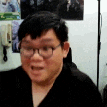 a man wearing glasses is making a funny face while sitting in front of a wall .