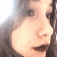 a close up of a woman 's face with a nose ring and dark lips .