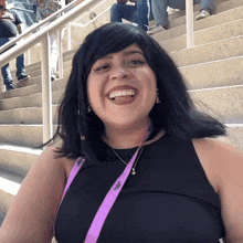 a woman wearing a black top and a purple lanyard that says ' a ' on it smiles