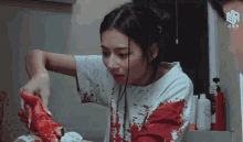 a woman in a bloody shirt holds a piece of meat in her hand