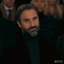 a man with a beard sits in a dark room with a netflix logo in the corner