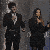 a man in a suit is holding a microphone next to a woman in a black jacket