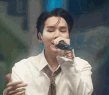a man in a white shirt and tie is singing into a microphone with his eyes closed .