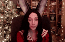 a woman wearing bunny ears is sitting in front of a bookshelf with a book titled ' a christmas carol '