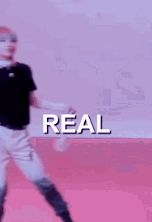 a man in a black shirt and white pants is dancing in front of a pink background with the word real written on it .