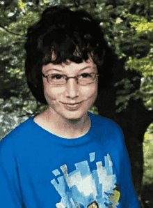 a young boy wearing glasses and a blue shirt is standing in front of trees .