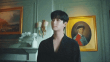 a young man in a black suit is standing in front of a painting on a wall .