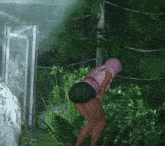 a woman in a pink top and black shorts stands in a lush green forest