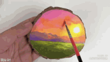 a person is painting a sunset on a piece of wood with wow art written on the bottom