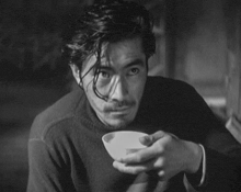 a black and white photo of a man holding a cup of coffee .