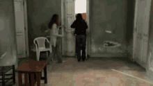 a woman in a black jacket is standing in a room with a white chair