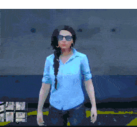 a woman in a blue shirt and sunglasses is standing in front of a blue wall .