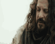 a man with long curly hair and a beard is wearing a fur coat and scarf .