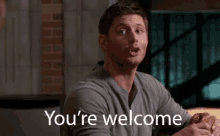 a man is sitting at a table with a sandwich in his hand and says `` you 're welcome '' .