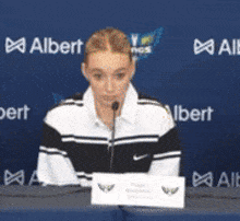 a woman is sitting at a table with a microphone in front of a albert sign