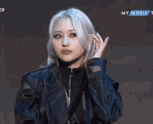 a woman with white hair and a black jacket is making a heart with her finger .
