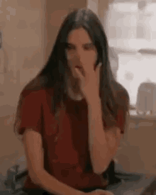 a woman with long hair is sitting at a desk with her hand on her nose .
