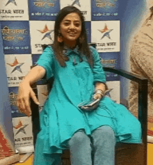 a woman in a blue dress is sitting in a chair holding a cellphone