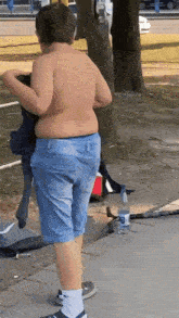 a shirtless boy in blue shorts is standing next to a bottle of aquafina water