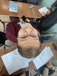 a person wearing glasses sits at a desk with papers and a book that says ' russian ' on it