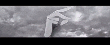 a black and white photo of a person 's hand pointing at a cloudy sky .