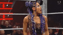 a woman with blue dreadlocks is screaming in a wrestling ring with a wwe logo in the background