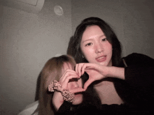two women are making a heart with their hands in a dark room