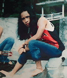 a person wearing a red and black shirt with the letter a on it sits on a rock
