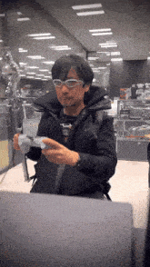 a man wearing glasses and a black vest holds a remote control