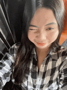 a woman in a black and white plaid shirt winks at the camera