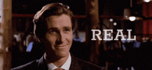 a man in a suit and tie smiles with the word real behind him
