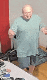 a bald man in a blue shirt and shorts is standing in front of a bed