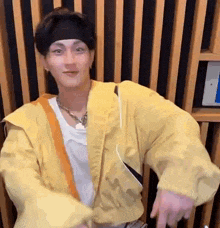 a young man wearing a yellow jacket and a headband is dancing in a room .