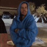 a man in a blue hoodie stands with his arms crossed in front of tents