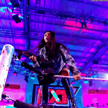 a woman is holding a rope in a wrestling ring with a x on the wall in the background