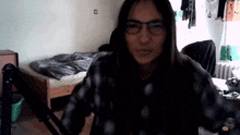 a woman wearing glasses and a plaid shirt is standing in front of a bed