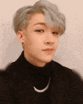a close up of a person wearing a black turtleneck and a silver chain