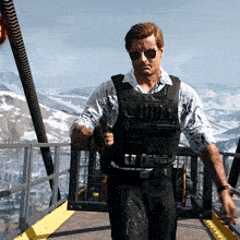 a man wearing sunglasses and a black vest with bullets on it stands on a bridge