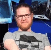 a man with a beard and glasses is sitting with his arms crossed in front of a wall .