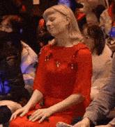 a woman in a red dress is sitting in the audience with her eyes closed .