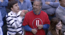 a man in a red shirt with the number 11 on it is talking to a boy in a crowd of people .